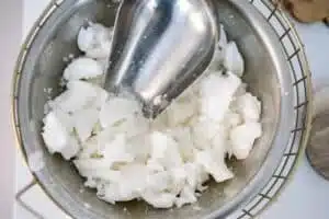 Scooper in a stainless steel bowl filled with chunks of soy candle wax.