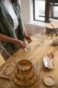 Person making candles indoors at a wooden table with crafting materials.